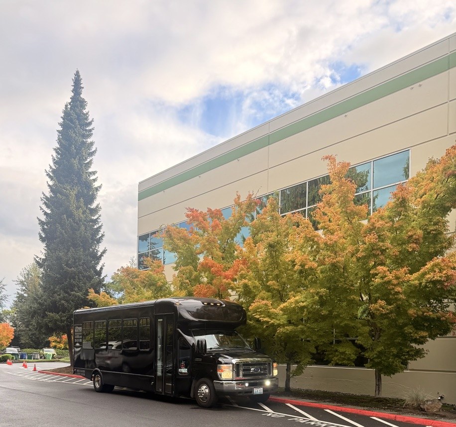 A Wayven shuttle bus parked outside a building lined with fall trees